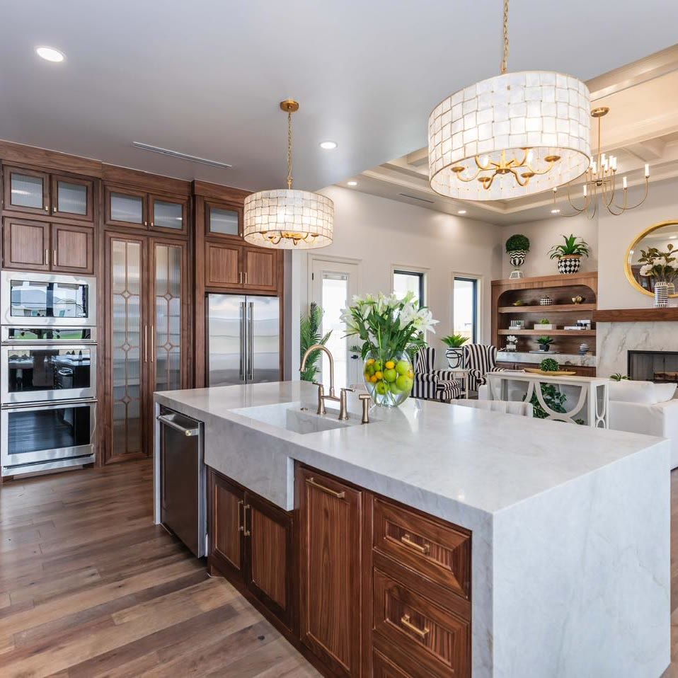 A kitchen with stained wood cabinets, a white waterfall island and two drum pendant lights.