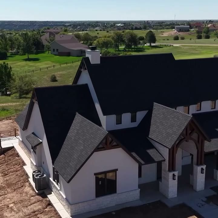 A white house with black roofs and black soffits seen from the air, a golf course behind it.