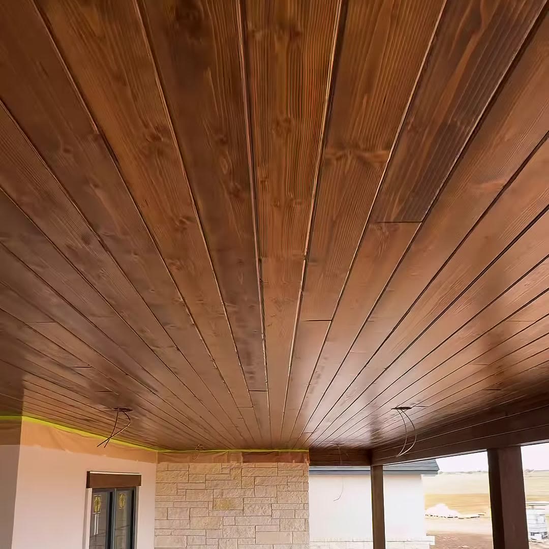 A porch ceiling of stained tongue-and-groove boards over a pale stone wall.