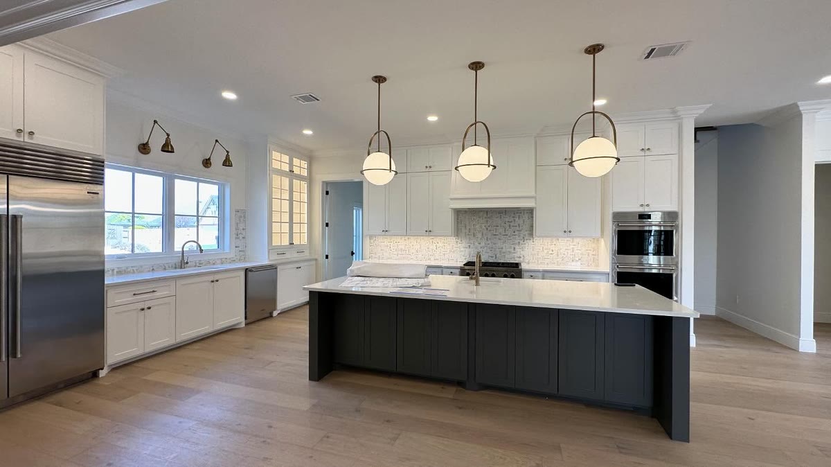 An open white kitchen with a black island and three pendant lights.