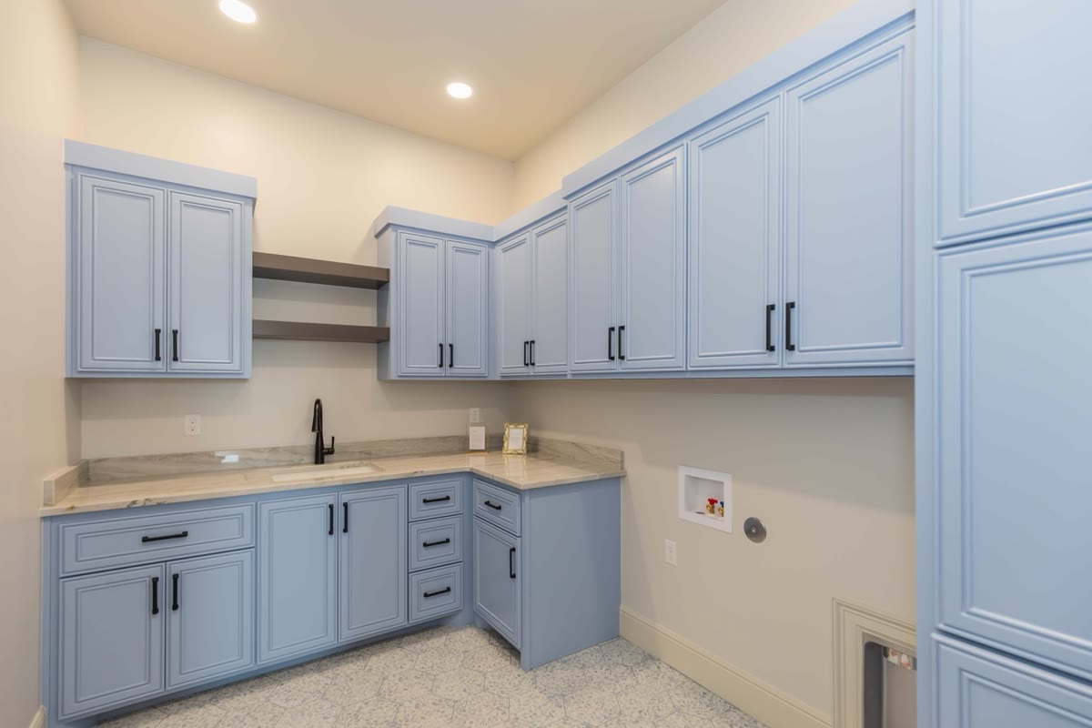 A laundry room with light blue cabinets, black handles and a butcher-block counter.