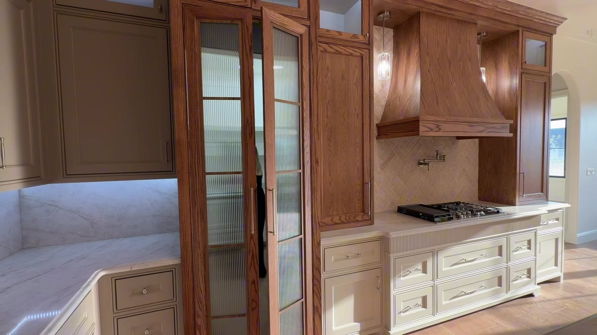 Stained wood cabinets with glass doors beside a white cabinet run and a range.