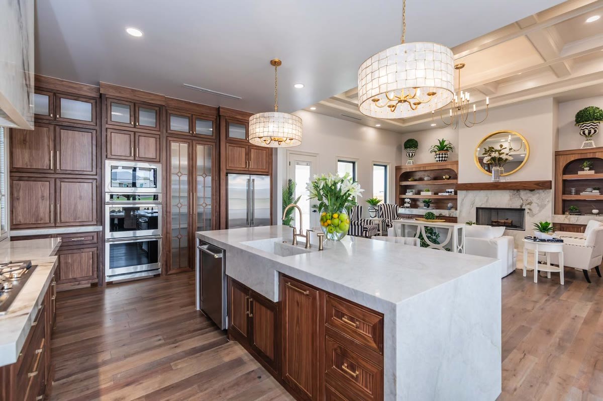 A kitchen with stained wood cabinets, a white waterfall island and two drum pendant lights.