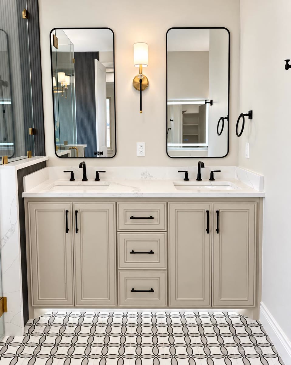 A double bathroom vanity in a warm taupe with black handles, under two black-framed mirrors.