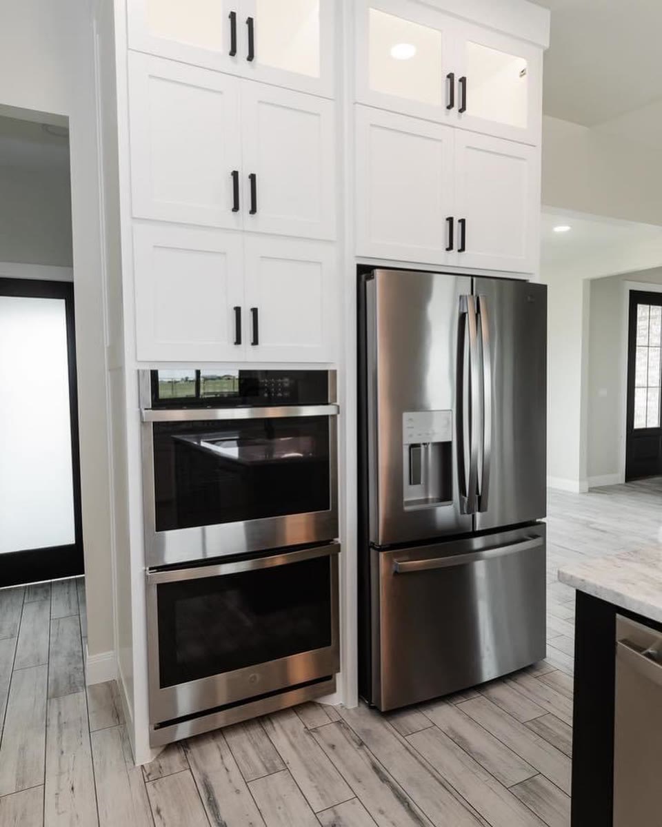 Tall white cabinets around a stainless double oven and refrigerator.
