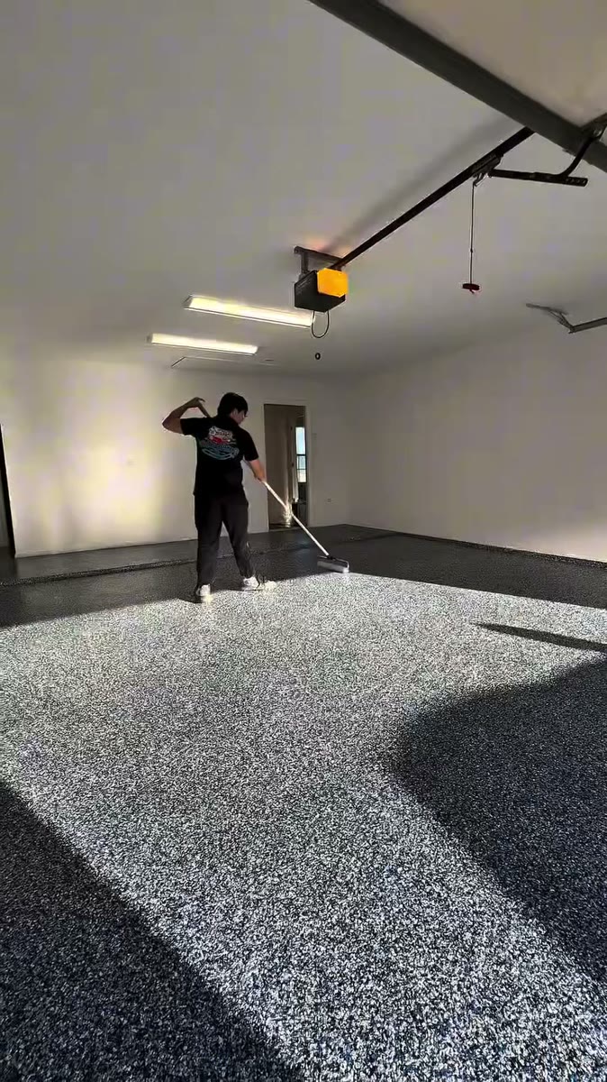 A painter working across a blue and grey flake epoxy garage floor.