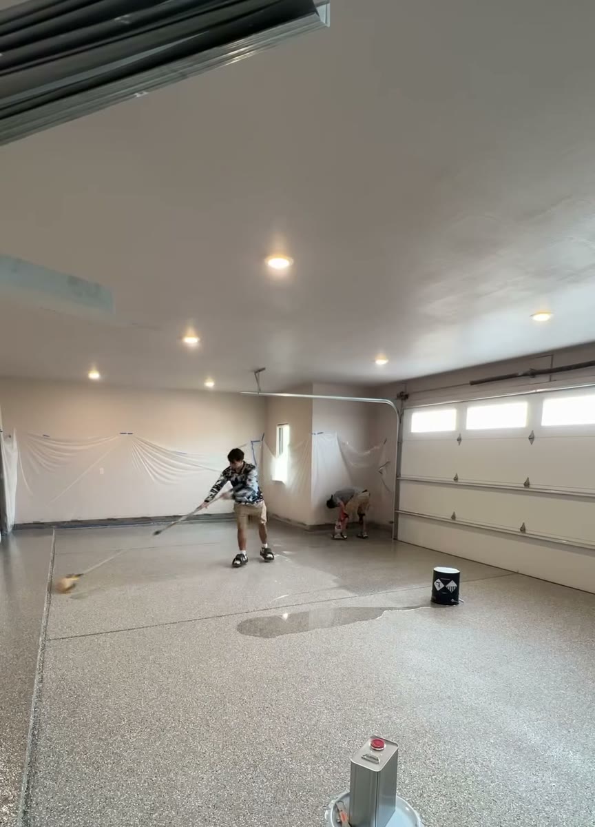 A large room with a new flake epoxy floor and a painter working at the far end.