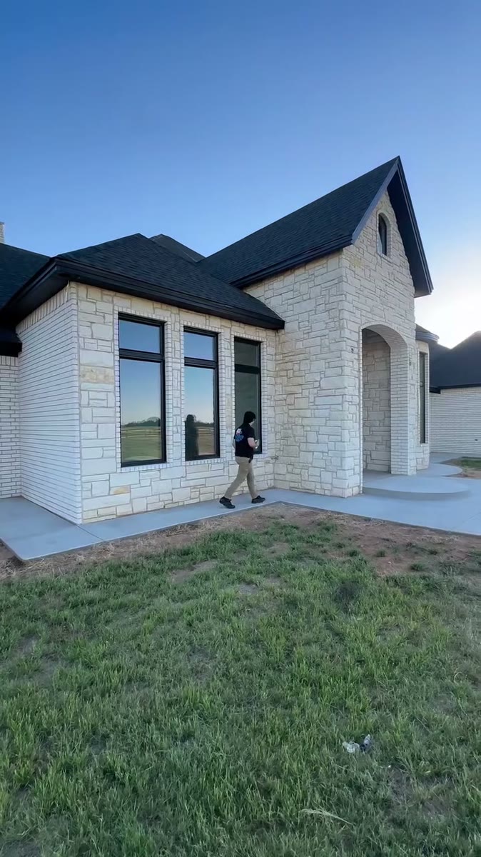 A pale stone house with black roofs and black window frames behind a green lawn.