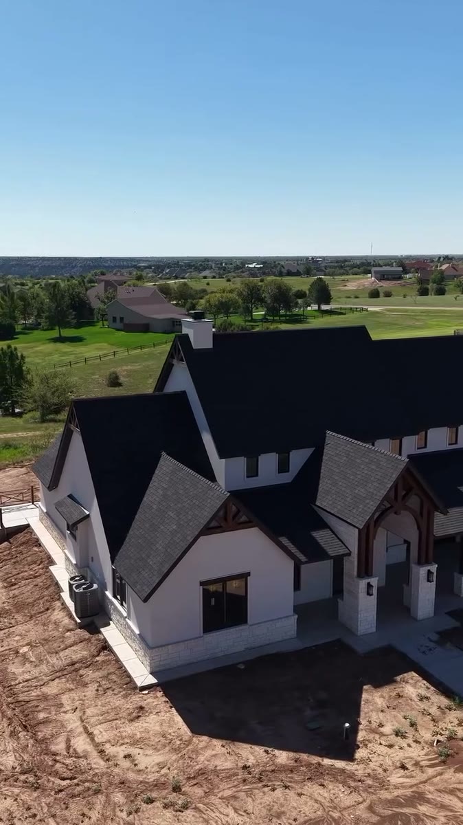 A white house with black roofs and black soffits seen from the air, a golf course behind it.