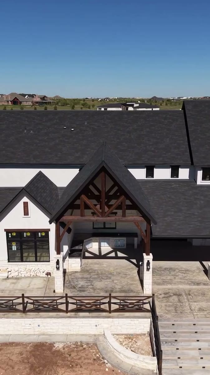 A covered back porch with stained cedar trusses on a white house with a black roof.