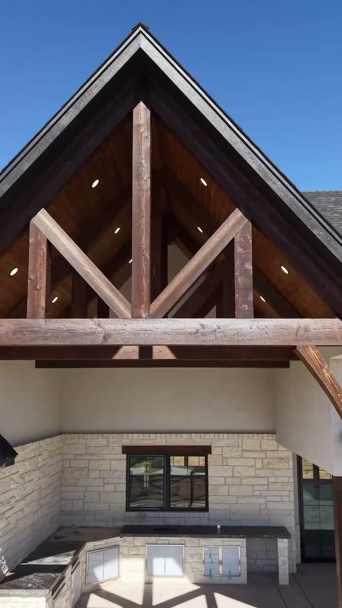 A gable porch of stained cedar trusses with a black soffit, under a blue sky.