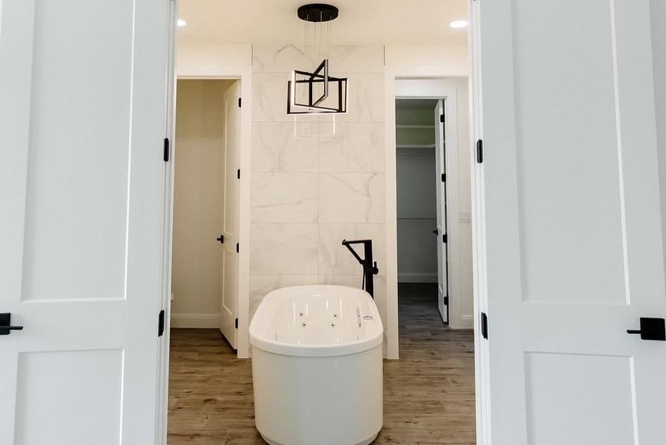 A white bathroom with a freestanding tub, black fixtures and a walk-in closet.