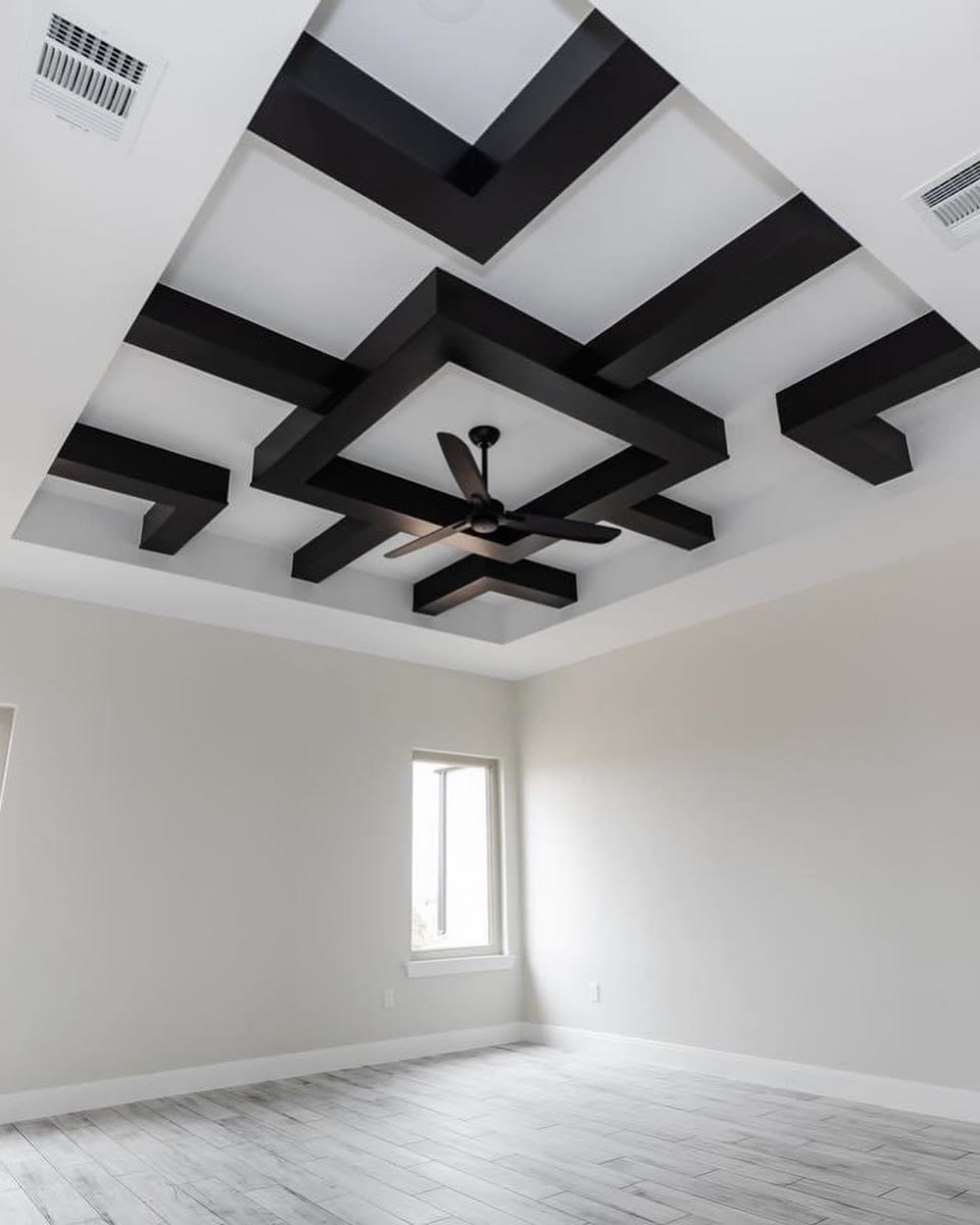 A white room with a geometric ceiling of black beams around a black ceiling fan.