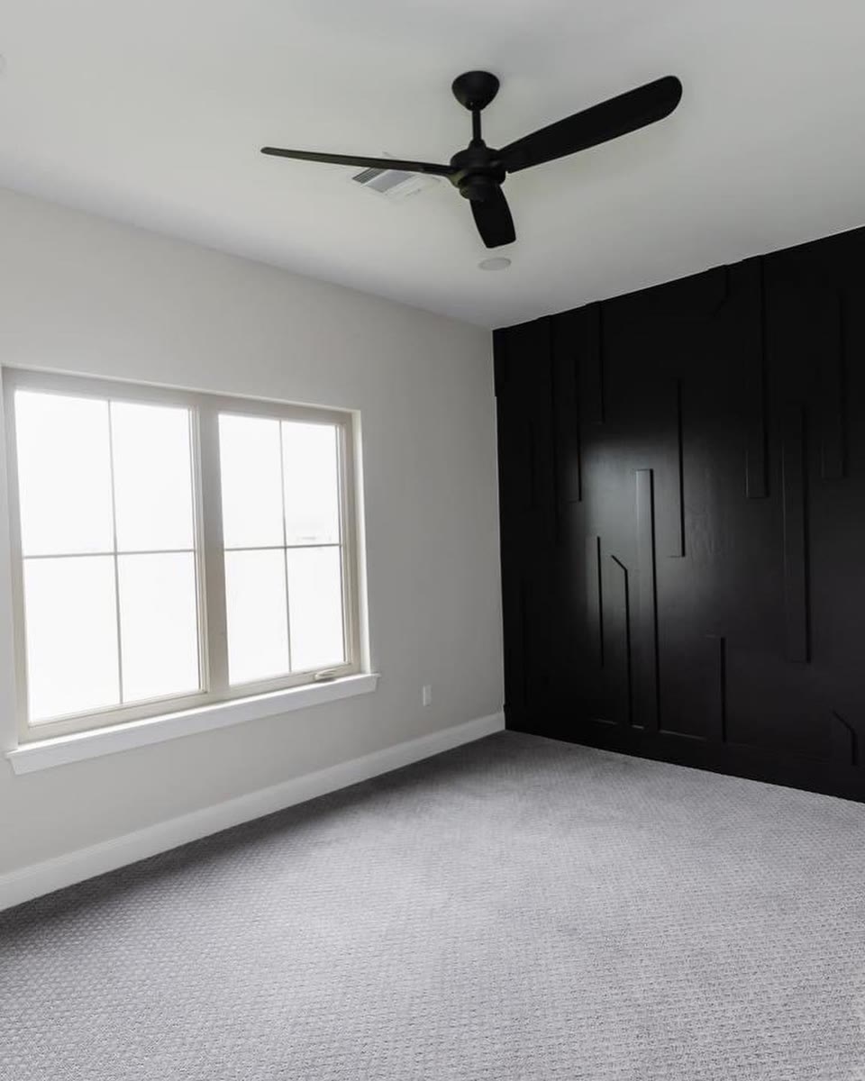 A white bedroom with a wall of black built-in wardrobes and a ceiling fan.