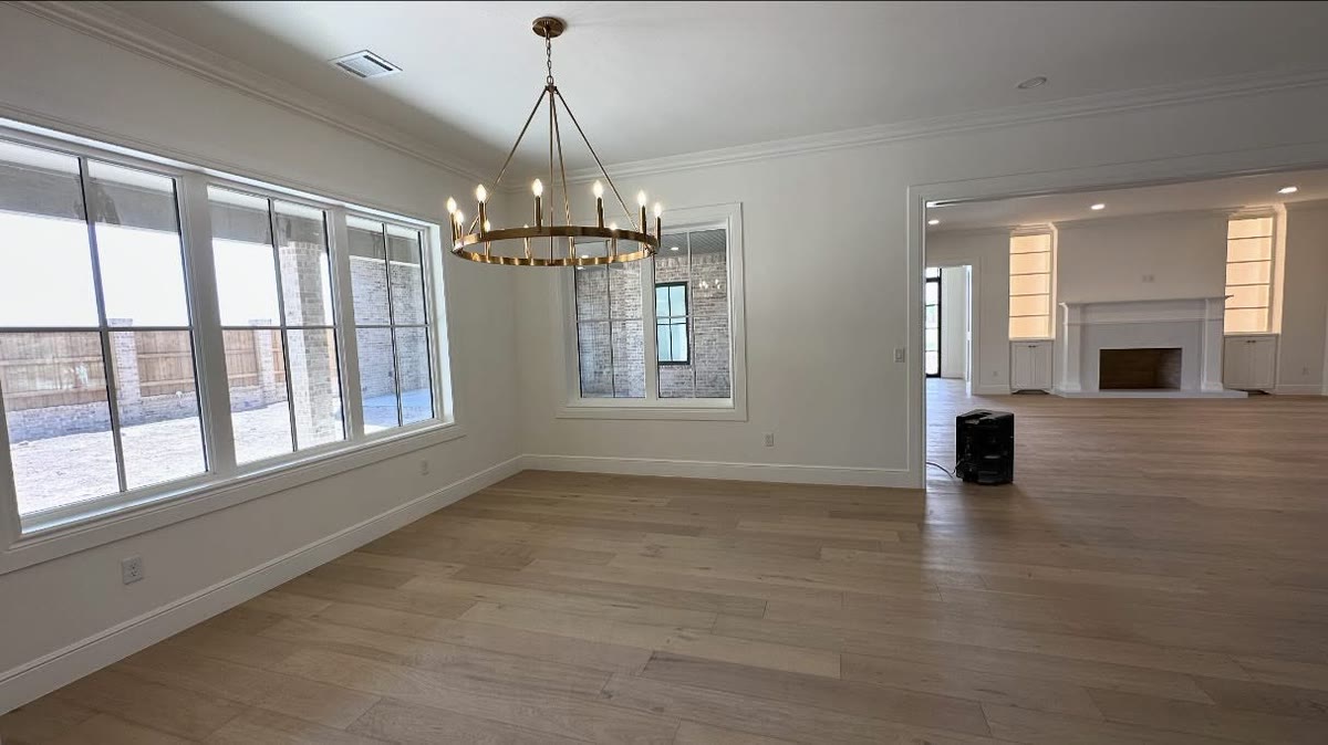 An open living room with a round chandelier, white walls and wood floors.
