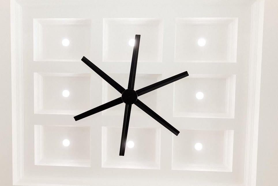 A white coffered ceiling with a black fan, over a grey floor.