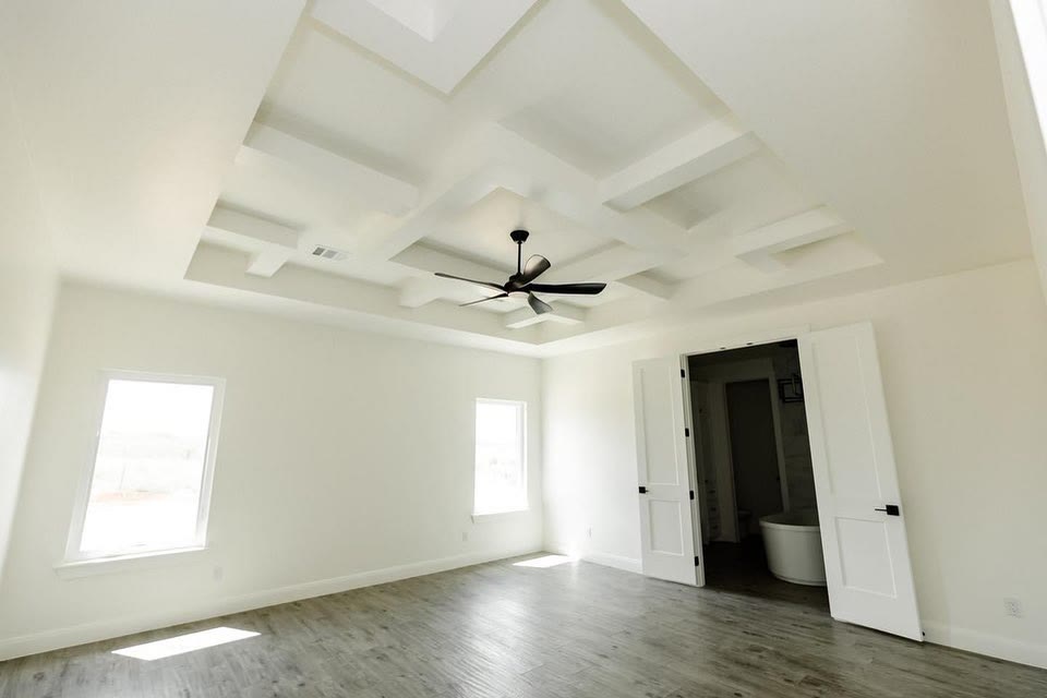A white living room with a coffered ceiling, grey floors and a black door.