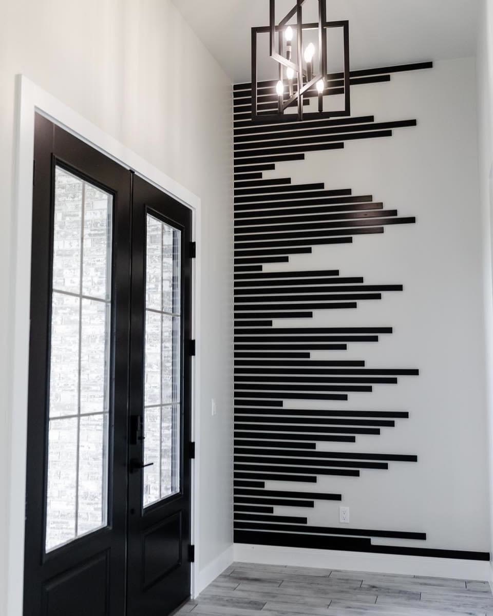 A tall white entry wall with black slats of different lengths beside black glass doors.