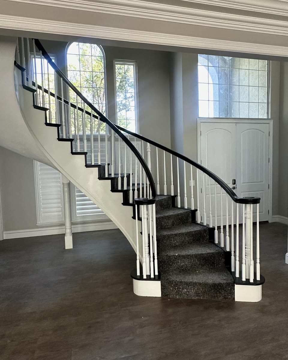 A curved staircase with white spindles and a black handrail in a two-storey entry.