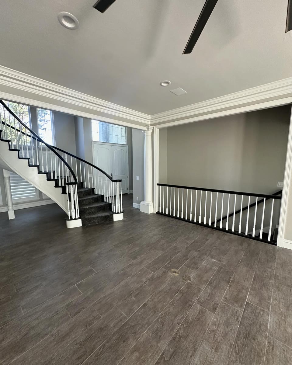 A stair landing with white spindles and a black handrail over dark wood floors.