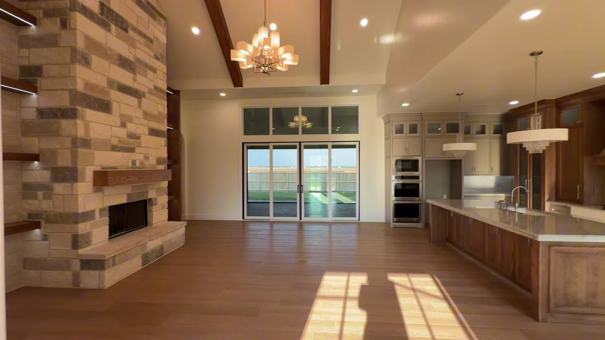 A long open room with a stacked-stone fireplace, wood beams and a glass chandelier.