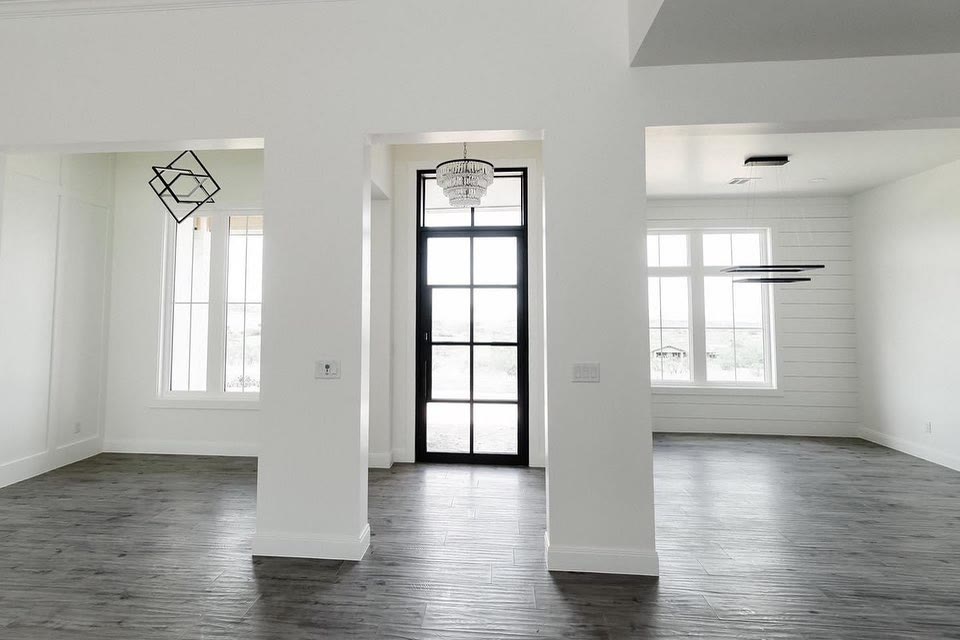 A white bedroom with a tall window and a black door.