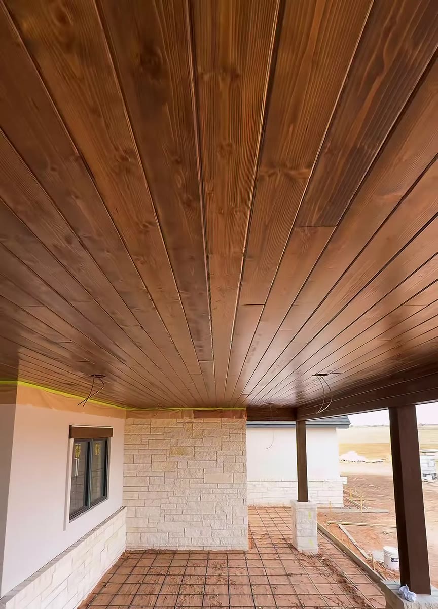 A porch ceiling of stained tongue-and-groove boards over a pale stone wall.