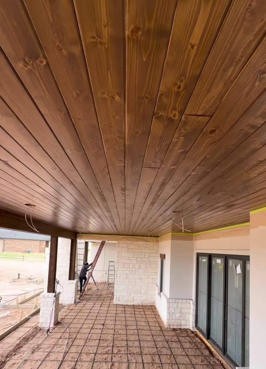 A long covered porch with a stained wood ceiling and stone columns.