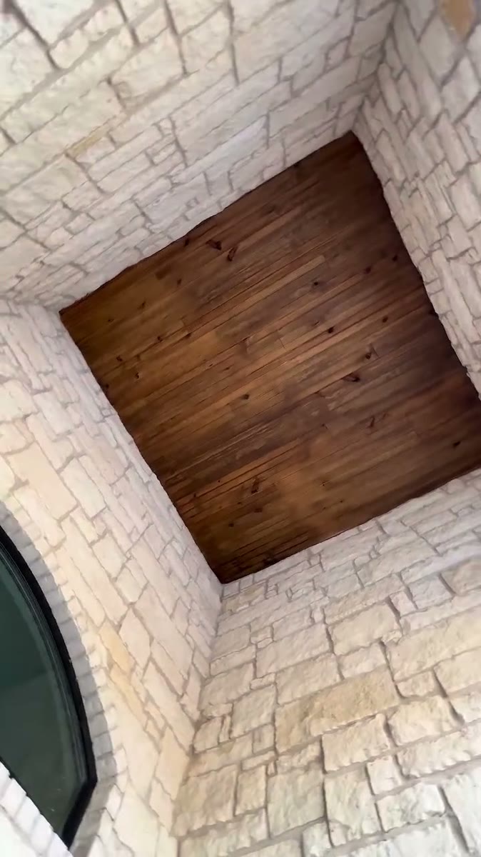 A small stained wood ceiling framed by pale stone walls, seen from below.
